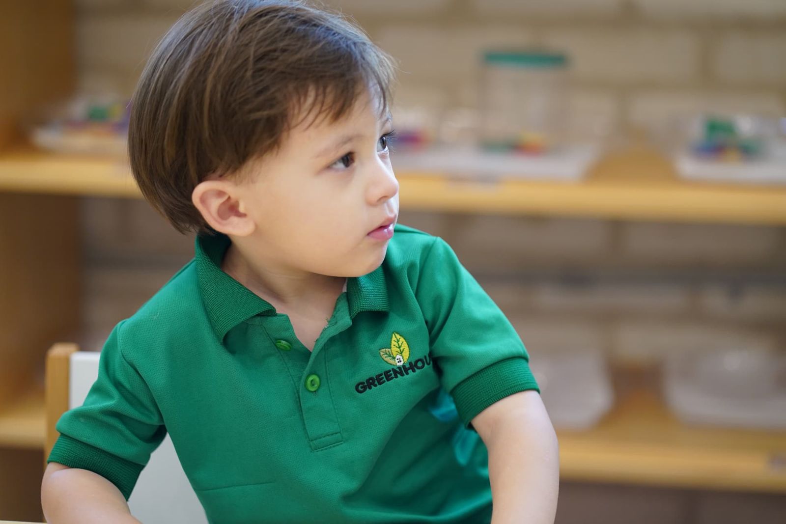 Niño de Pre-K bilingüe con polo verde de Greenhouse en su salón de clases