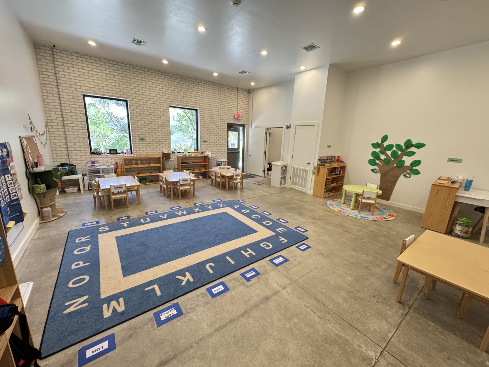 Salón de Pre-K de Greenhouse McAllen con tapete del abecedario y mesas de madera